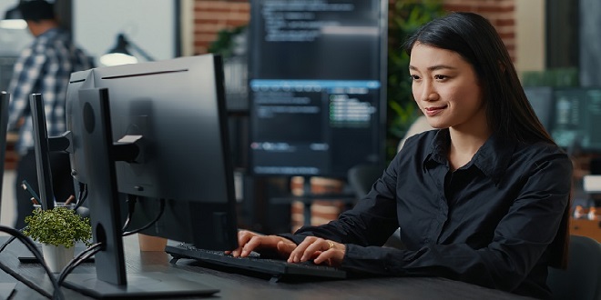 Portrait of smiling asian programer focused on writing code sitting at desk in software development office. System engineer concentrating on creating algorithm for it startup company.