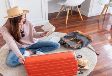 Young asian woman traveler prepare things into orange suitcase for holiday vacation at home.backpacker travel concept