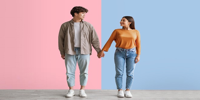 Full length portrait of millennial Asian couple smiling and looking at each other, holding hands, standing against white studio wall. Affectionate young man and woman being in love
