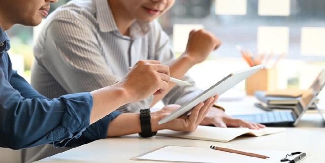 Cropped image of smart men working as project manager discussing/talking about their project by using a computer tablet while sitting together at the long white desk over glass wall as background.